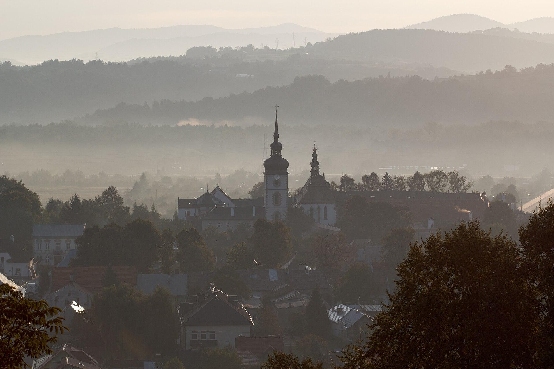 Panorama Starego Sącza we mgle, z wieżami kościołów i Beskidem Sądeckim w tle